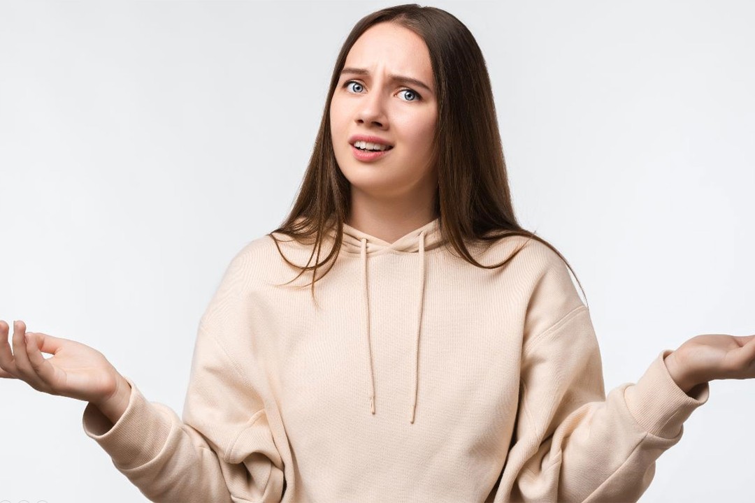  Junge Frau schaut verzweifelt fragend, hebt mit ungläubigen Blick die Hände 